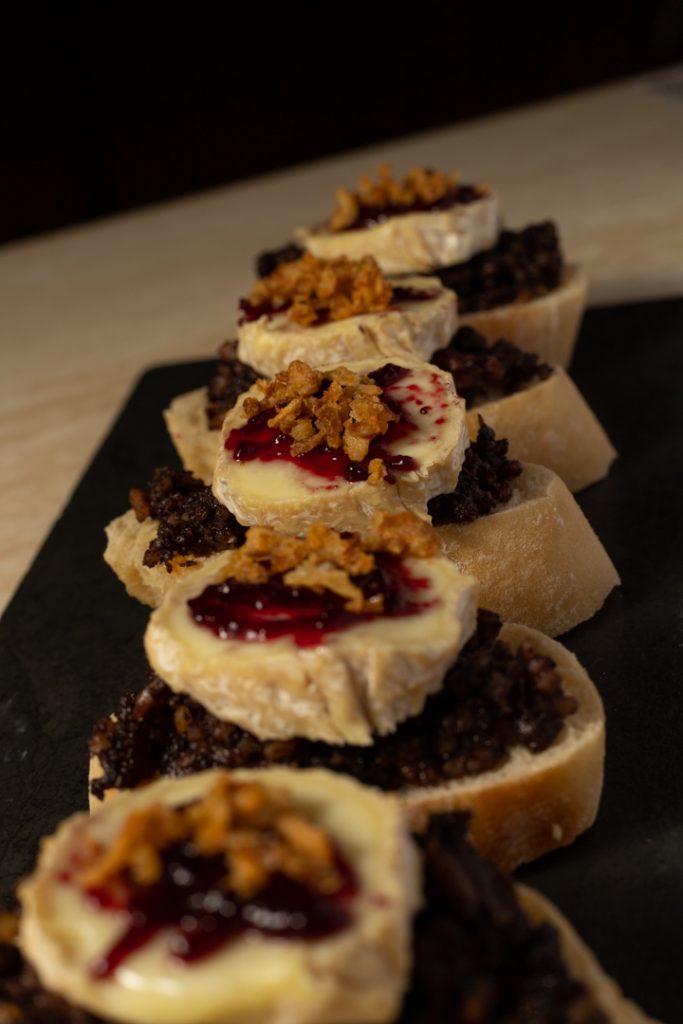 Tapa de morcilla con queso de cabra, mermelada de fresa y cebolla caramelizada encima de un pan Fotografo y videografo de gastronomia en Alicante